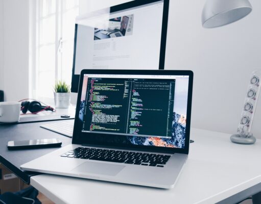 Code Bole Keyboardla – कोड बोले कीबोर्डला A MacBook with lines of code on its screen on a busy desk